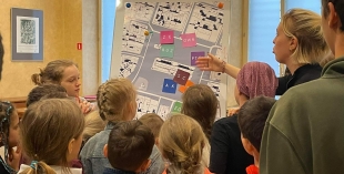 Na zdjęciu dzieci przyglądajcie się planszy, na którą wskazuje prowadząca zajęcia - Hanna Martynenko. 