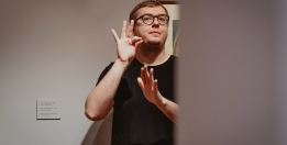 The photograph shows a man using sign language.