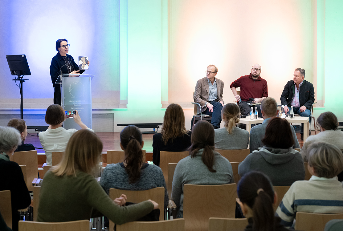 Sala Pod Kruki. Na scenie Agata Wąsowska-Pawlik przemawia. Prezentuje publiczności książkę 