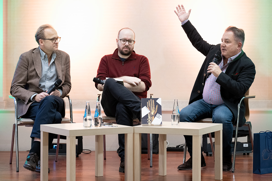 Na scenie siedzą: Maciej Czerwiński, w środku Grzegorz Wysocki, obok przemawiający i gestykulujący Robert Makłowicz.