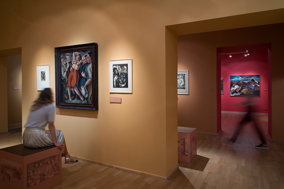 Wystawa Koszycka moderna pomarańczowe i czerwone ściany Galerii MCK, na nich obrazy czeskich artystów, na pierwszym planie osoba siedząca przed obrazem, na drugim ktoś przechodzący, rozmazany.