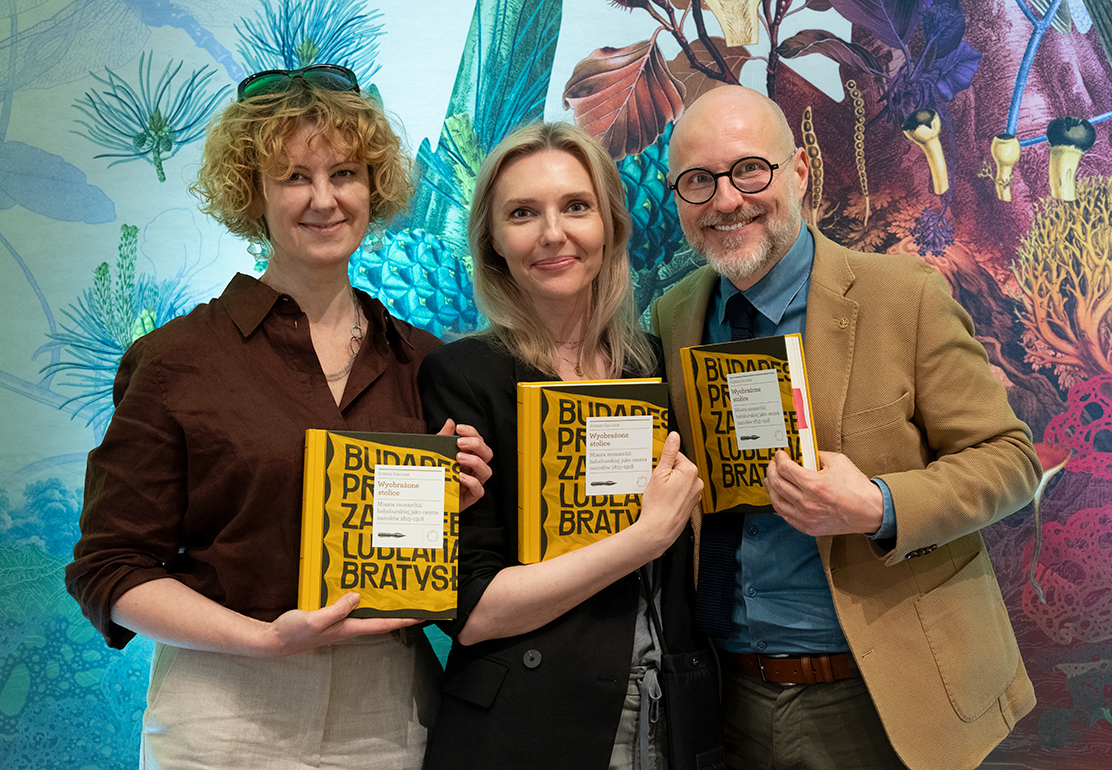 Marzena Daszewska, Paulina Orłowska-Bańdo i dr Łukasz Galusek pozują do wspólnego zdjęcia po spotkaniu autorskim w Międzynarodowym Centrum Kultury. Każda z osób trzyma egzemplarz książki Wyobrażone stolice. W tle widoczna jest kolorowa dekoracja ścienna.