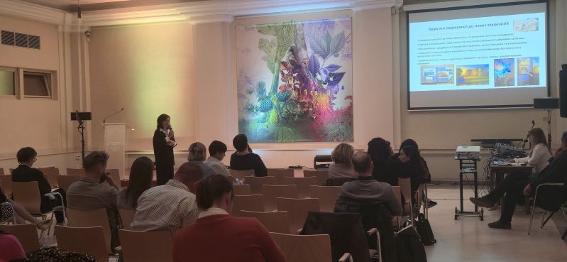 A speaker with a microphone gives a presentation to participants in the Pod Kruki Hall at the International Cultural Centre. The screen shows a Ukrainian-language slide about the use of new technologies, including in the presentation and preservation of heritage.