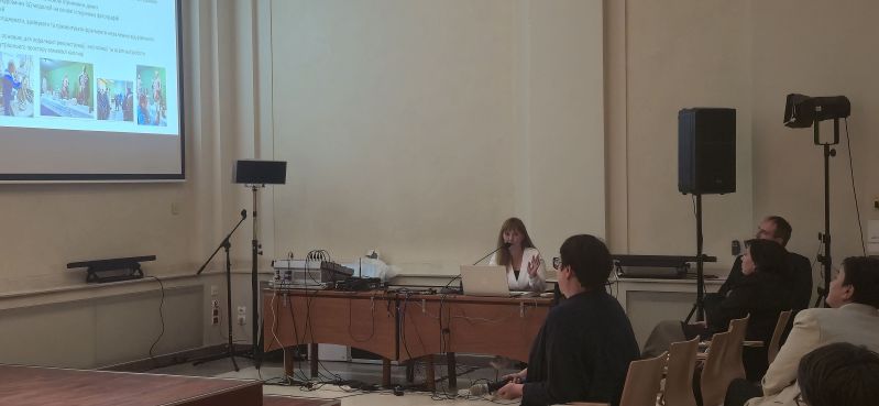 A speaker sits at a table with a laptop and microphone, giving a presentation to participants in the Pod Kruki Hall at the International Cultural Centre. The screen shows a Ukrainian-language slide about creating 3D models, photographic documentation and the digital reconstruction of heritage objects.
