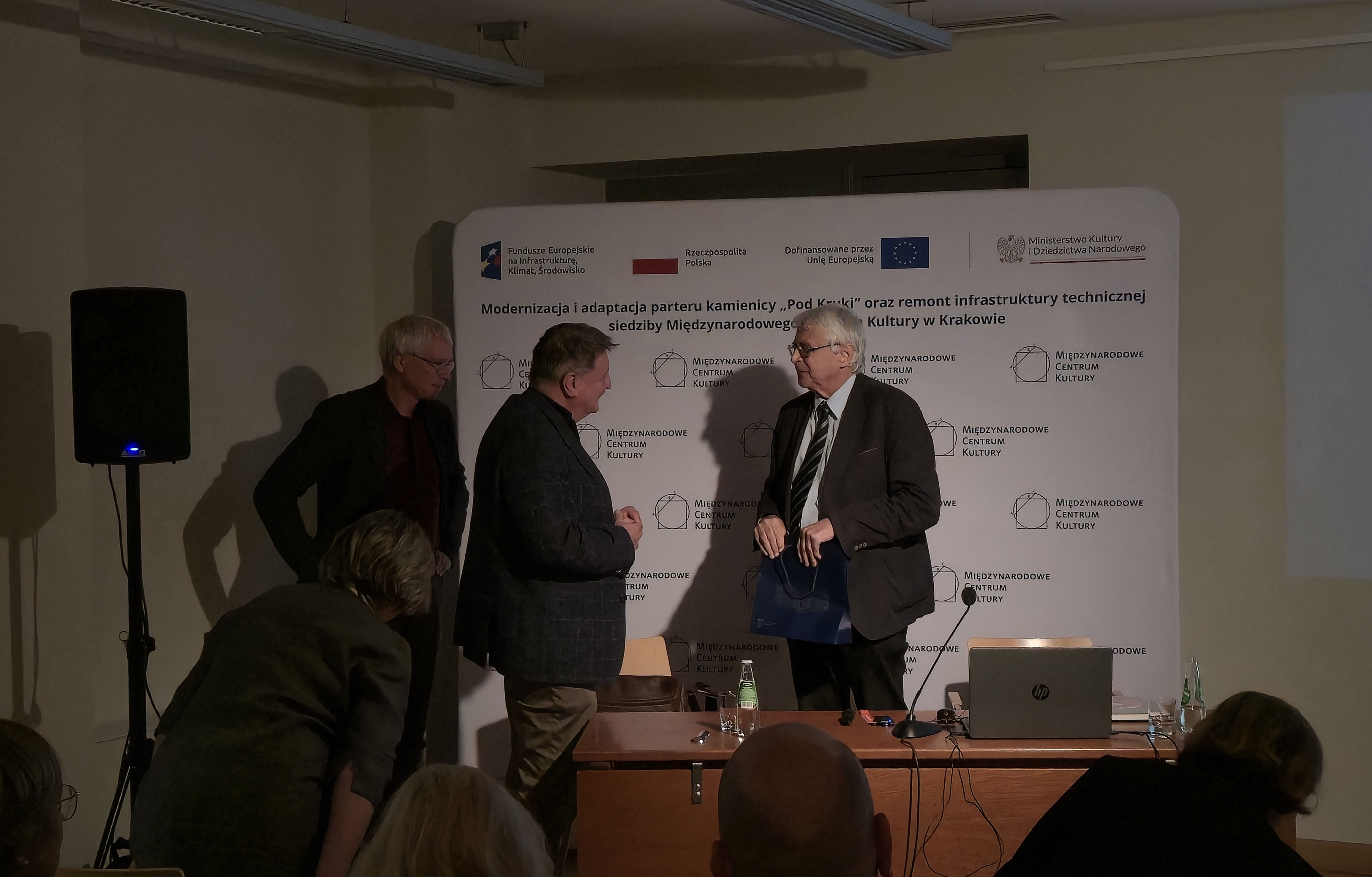Prof. Jacek Purchla podczas spotkania z delegacją z Hesji w siedzibie Międzynarodowego Centrum Kultury w Krakowie. Po zakończeniu prezentacji wręcza upominek jednemu z przedstawicieli delegacji, w obecności pozostałych uczestników spotkania.