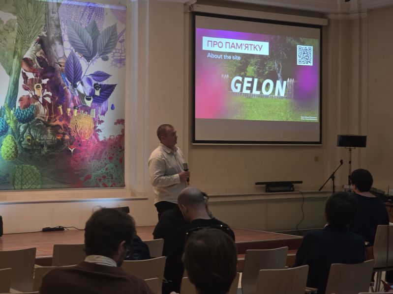 A speaker with a microphone presents a slide about GELON to the audience. A projection screen and a colourful installation are visible in the Pod Kruki Hall at the International Cultural Centre.