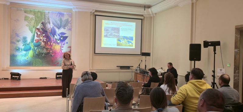 A speaker with a microphone gives a presentation to participants in the Pod Kruki Hall at the International Cultural Centre. The screen shows a Ukrainian-language slide about the Bohdan Khmelnytsky Museum and the Chyhyryn National Historical and Cultural Reserve.