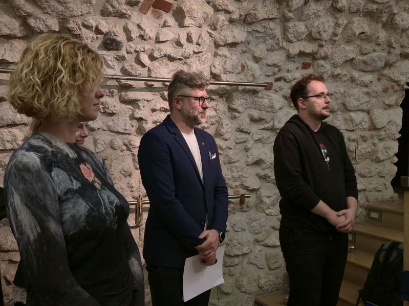 Marzena Daszewska wraz z uczestnikami IV Akademii Dziedzictwa dla Ukrainy podczas spotkania poświęconego sztucznej inteligencji i nowym technologiom w instytucjach kultury. Uczestnicy stoją w zabytkowym wnętrzu z kamiennymi ścianami i słuchają wystąpienia.