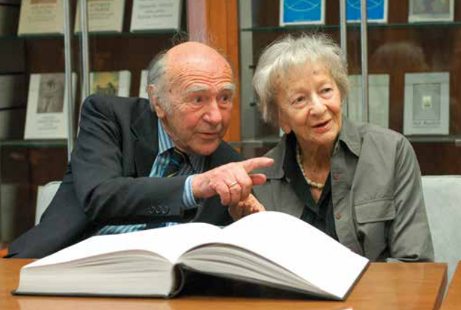 Karl Dedecius i Wisława Szymborska podczas spotkania w Międzynarodowym Centrum Kultury w Krakowie w 2005 roku. Siedzą przy stole nad otwartą książką, a Karl Dedecius wskazuje ręką w bok.