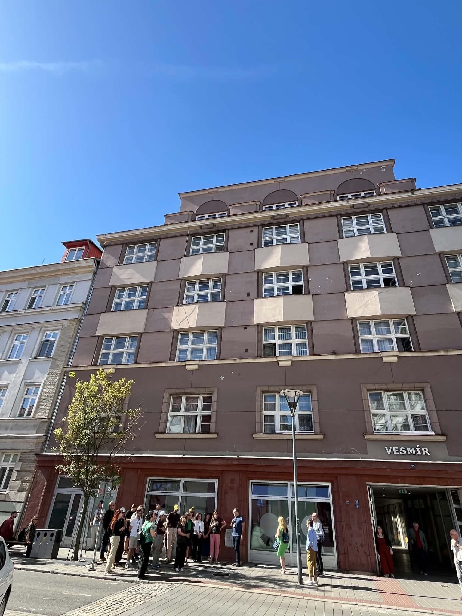 Uczestnicy seminarium objazdowego Europa Środkowa od środka przed budynkiem Vesmír w Ostrawie w Czechach. Grupa stoi na chodniku przed modernistyczną fasadą budynku podczas zwiedzania miasta.