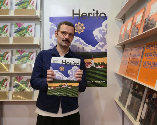 Bartosz Sadulski, redaktor naczelny magazynu HERITO, na stoisku Międzynarodowego Centrum Kultury podczas Gdańskich Targów Książki 2026. Trzyma w dłoniach najnowszy numer magazynu HERITO, prezentowany na tle ekspozycji publikacji MCK.