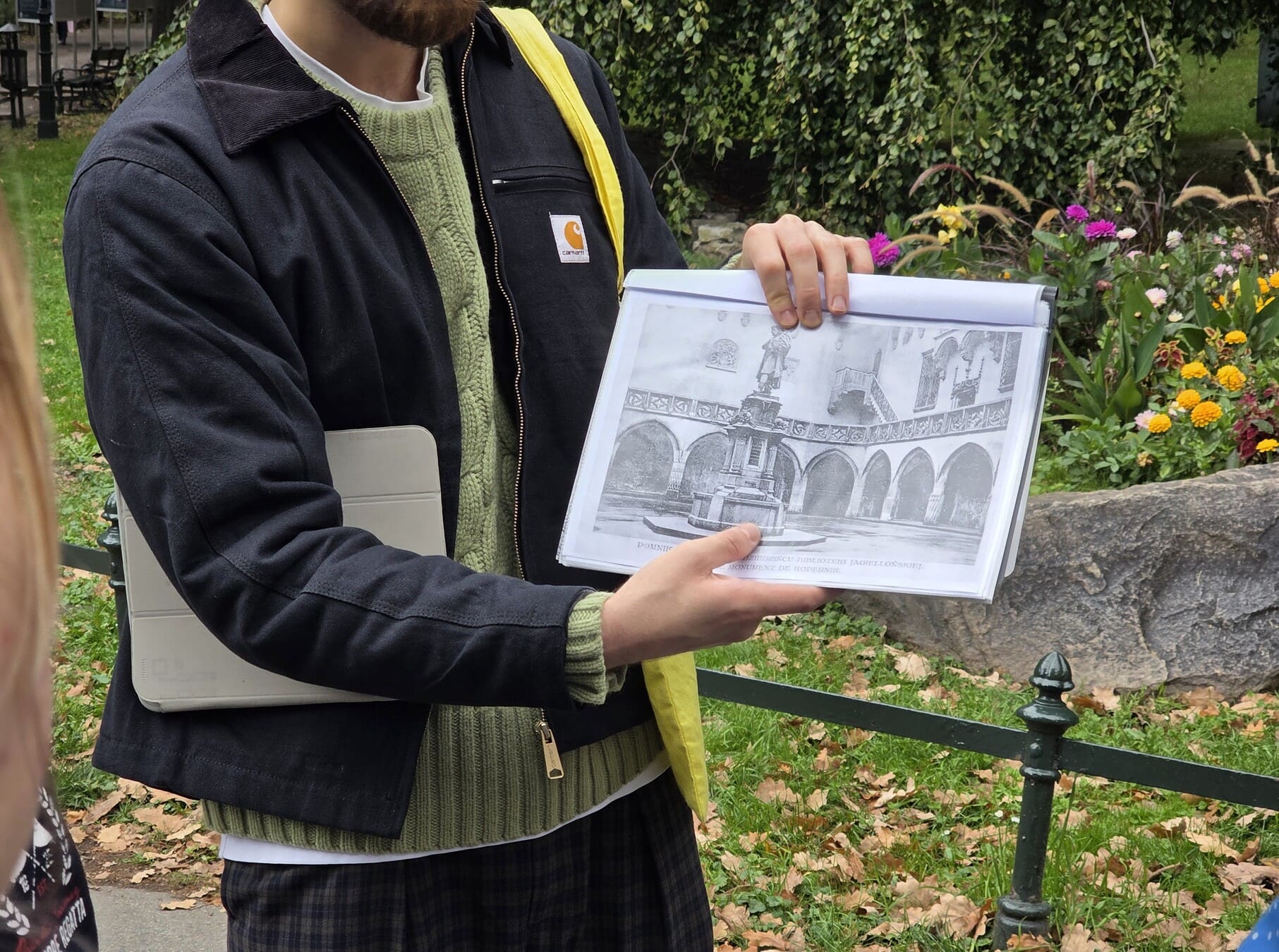 Marcin Krotla prowadzi spacer po krakowskich Plantach w ramach Festiwalu Kultury bez Barier dla osób z Teatru Drużyna. Pokazuje uczestnikom historyczną ilustrację jednego z krakowskich miejsc i opowiada o jego przeszłości.