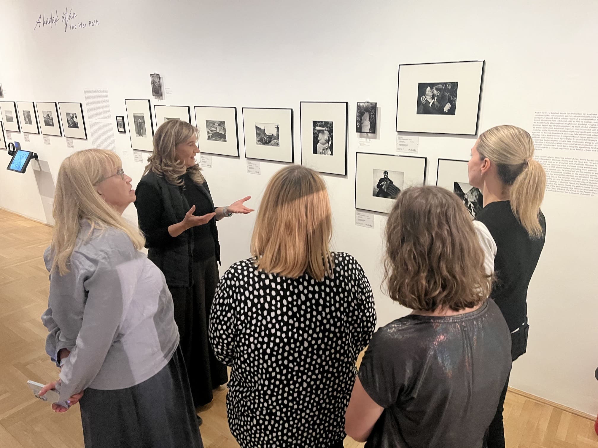 Przedstawicielki Międzynarodowego Centrum Kultury podczas wizyty studyjnej w jednej z budapeszteńskich instytucji wystawienniczych. Grupa ogląda ekspozycję fotograficzną The War Path; jedna z kobiet omawia prezentowane na ścianie czarno-białe fotografie.