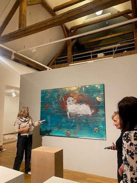 Przedstawicielki Międzynarodowego Centrum Kultury podczas wizyty studyjnej w Muzeum Sztuki w Ołomuńcu. Jedna z pracownic muzeum omawia obraz prezentowany na ścianie, wskazując jego elementy, a uczestniczki seminarium słuchają w sali wystawowej z widoczną drewnianą konstrukcją dachu.